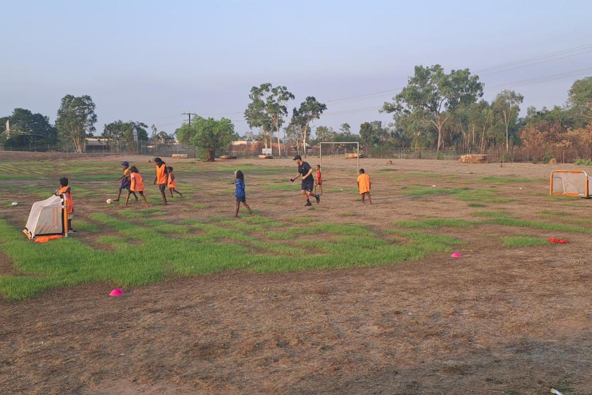 Young children playing football on a school oval at dusk