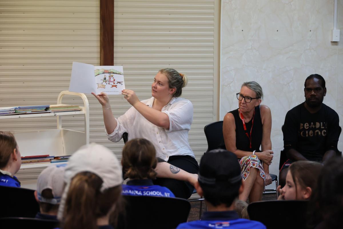 A lady in a white shirt reading a book to audience