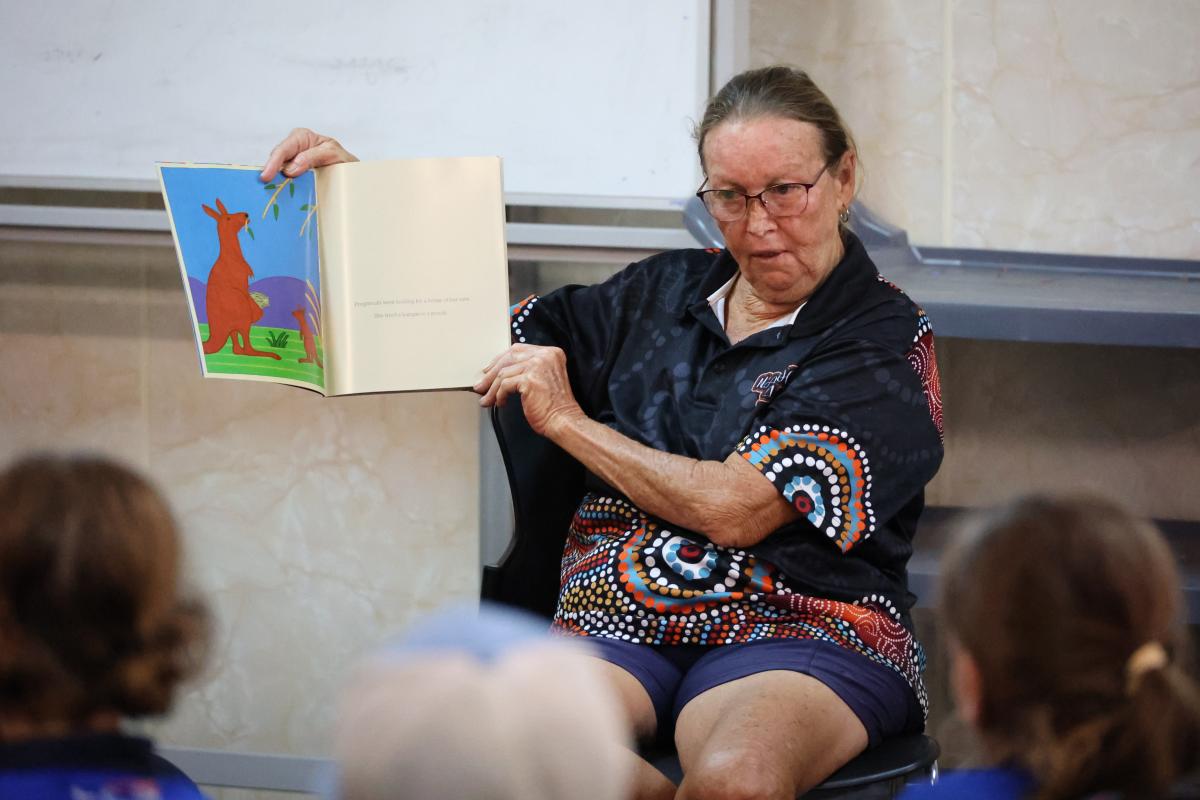 A women holding up a children's book and reading to audience