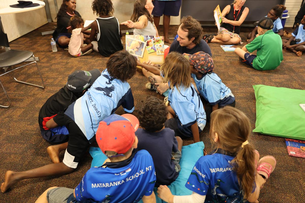 Group of students and teacher reading a book on the floor