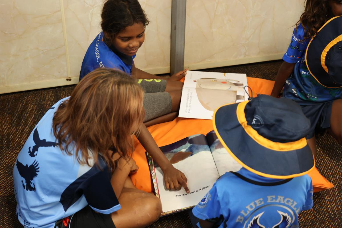 3 students reading a book on the floor