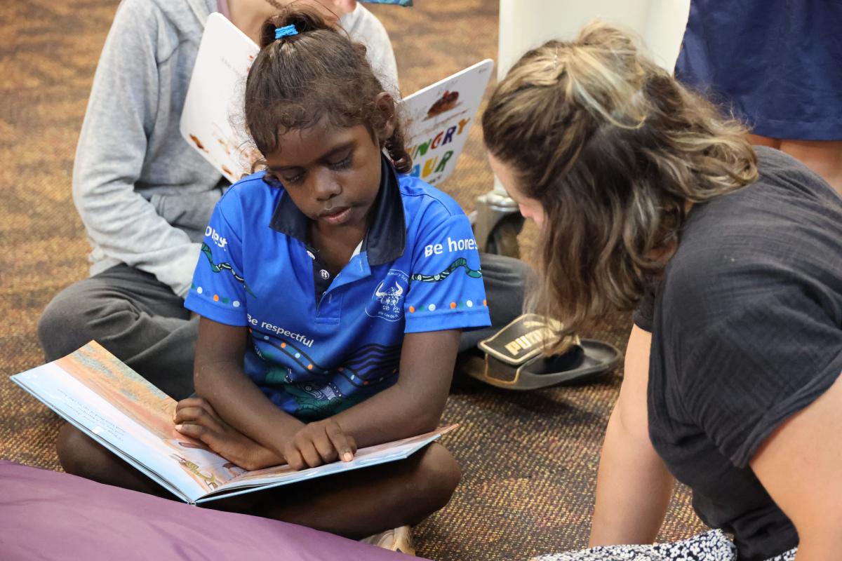 A teacher and student reading a book on the floor