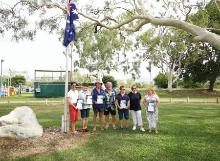 Seven award recipients standing under Australian flag