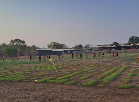 Young children playing football on a school oval at dusk