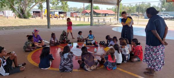 Children sitting on basketball court drawing pictures