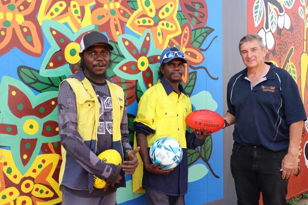 Three people holding footballs in front of a colourful mural